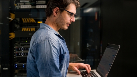 White male IT professional working on laptop in data center server room
