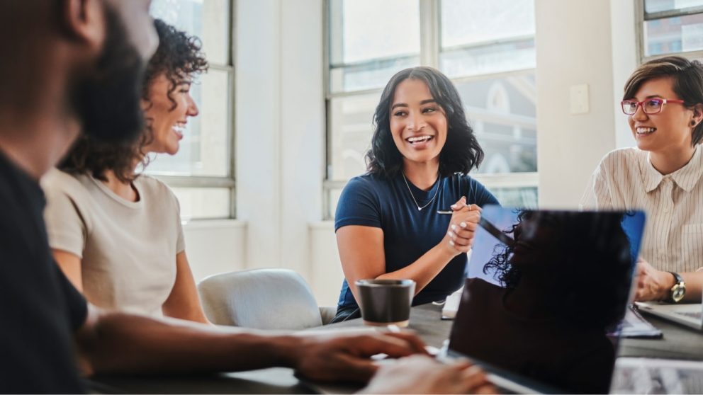 Three young professional women of mixed ethnicities and African American man talking at table.