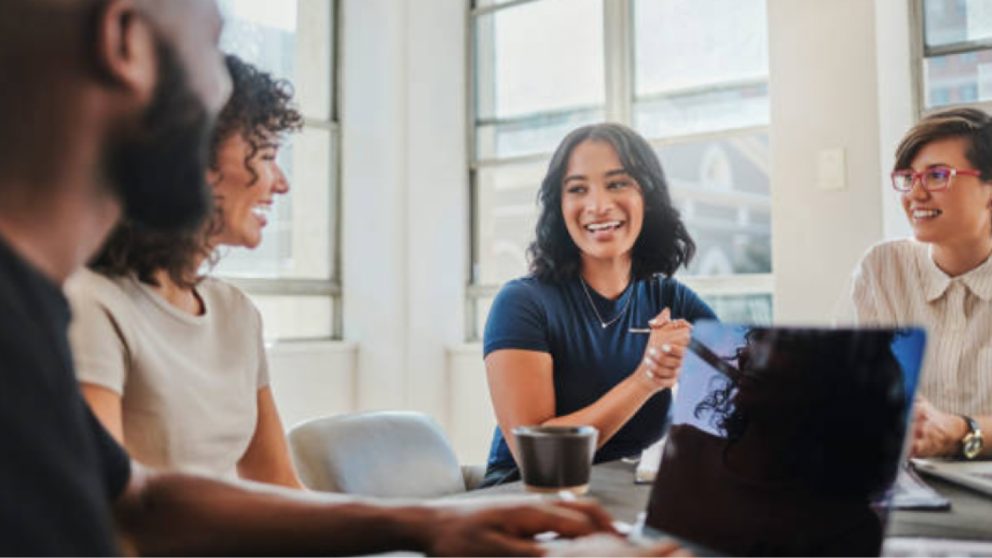 Three young professional women of mixed ethnicities and African American man talking at table.