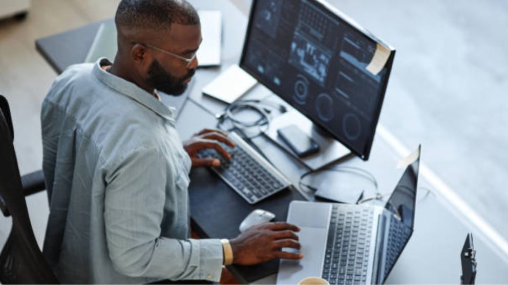 African American man working on laptop and desktop at the same time.