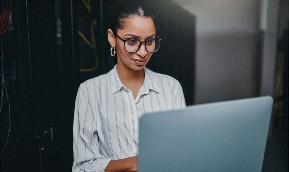 Woman with glasses working at computer in data center.