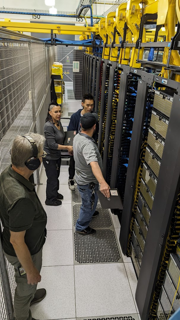 Summit engineers walking a row of server cabinets under yellow cable trays